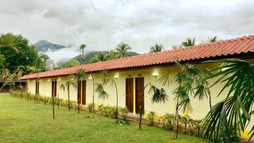 A row of yellow buildings with red roofs, surrounded by grass and palm trees, under a cloudy sky.