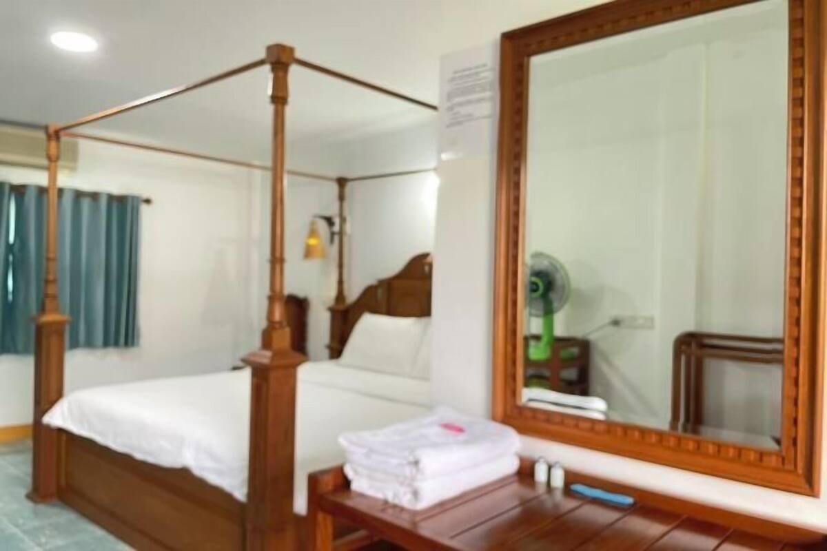 A four-poster bed with a wooden frame, a large mirror with a wooden frame, and a bedside table with a folded white towel and a blue pen.