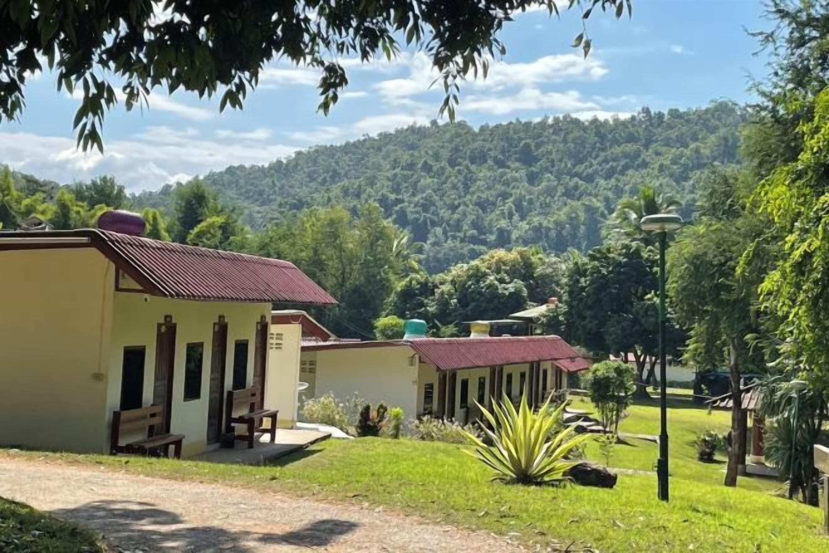 A building with a red roof, a covered outdoor seating area, and a view of a forested hill.