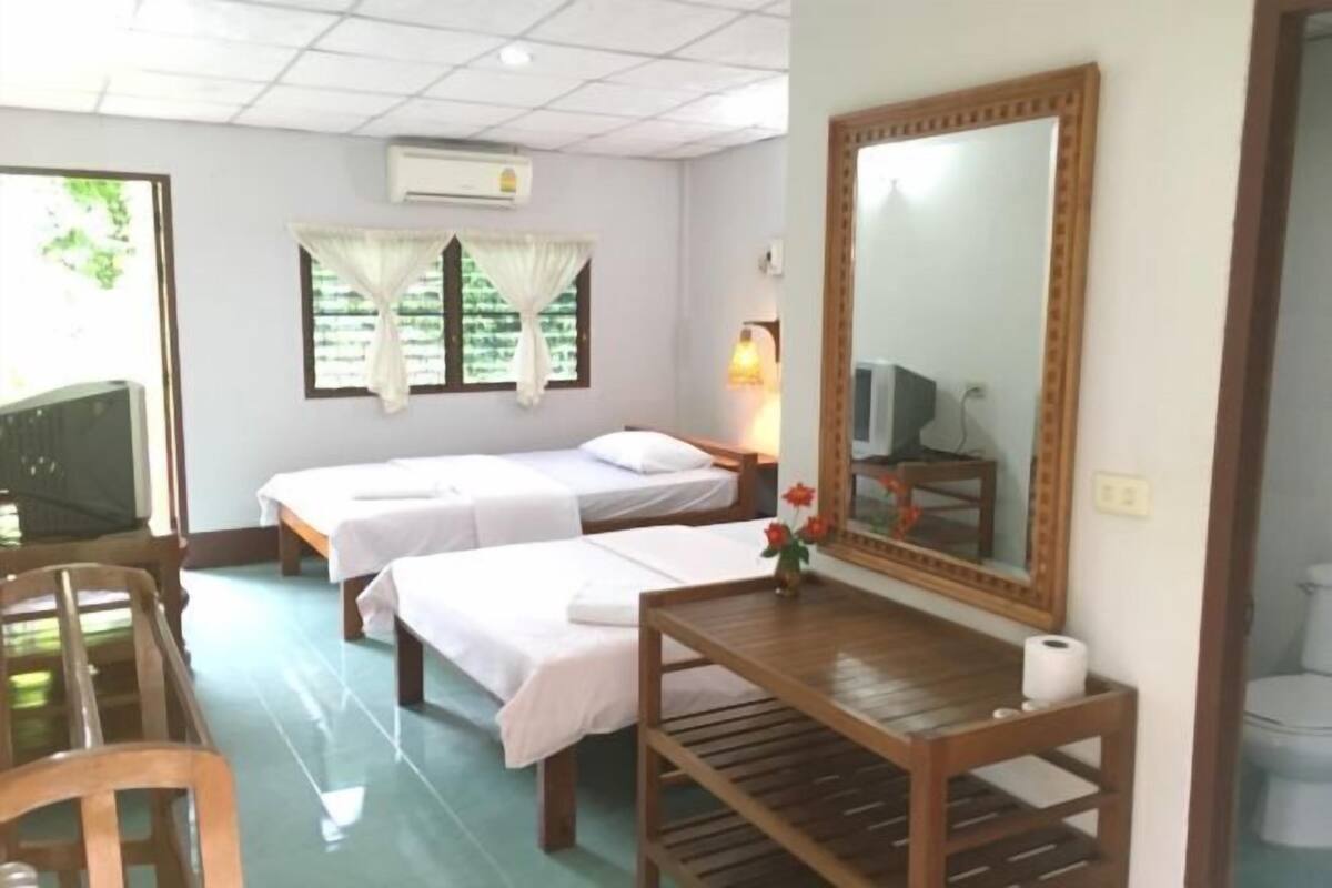 A room with two single beds, a wooden table with a mirror, a chair, and a TV.