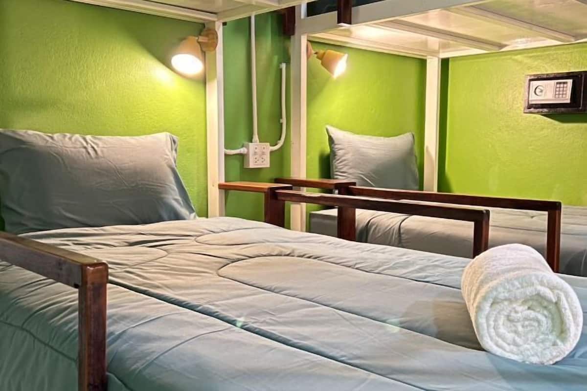 Een eenpersoonsbed met houten frame, een witte handdoek en een bedieningspaneel aan de muur.