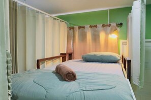 Un lit simple avec une serviette roulée, une table de chevet et une petite table de nuit avec une lampe.