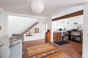 A modern living room with a grey sofa, a staircase, a kitchen area, and a large window.