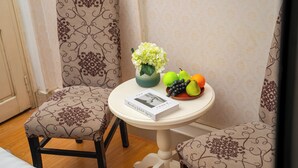 A room with two patterned chairs, a small round table with a book, a vase with flowers, and a bowl of fruit. - Hanoi Old quarter Central Hotel (Hanoi)