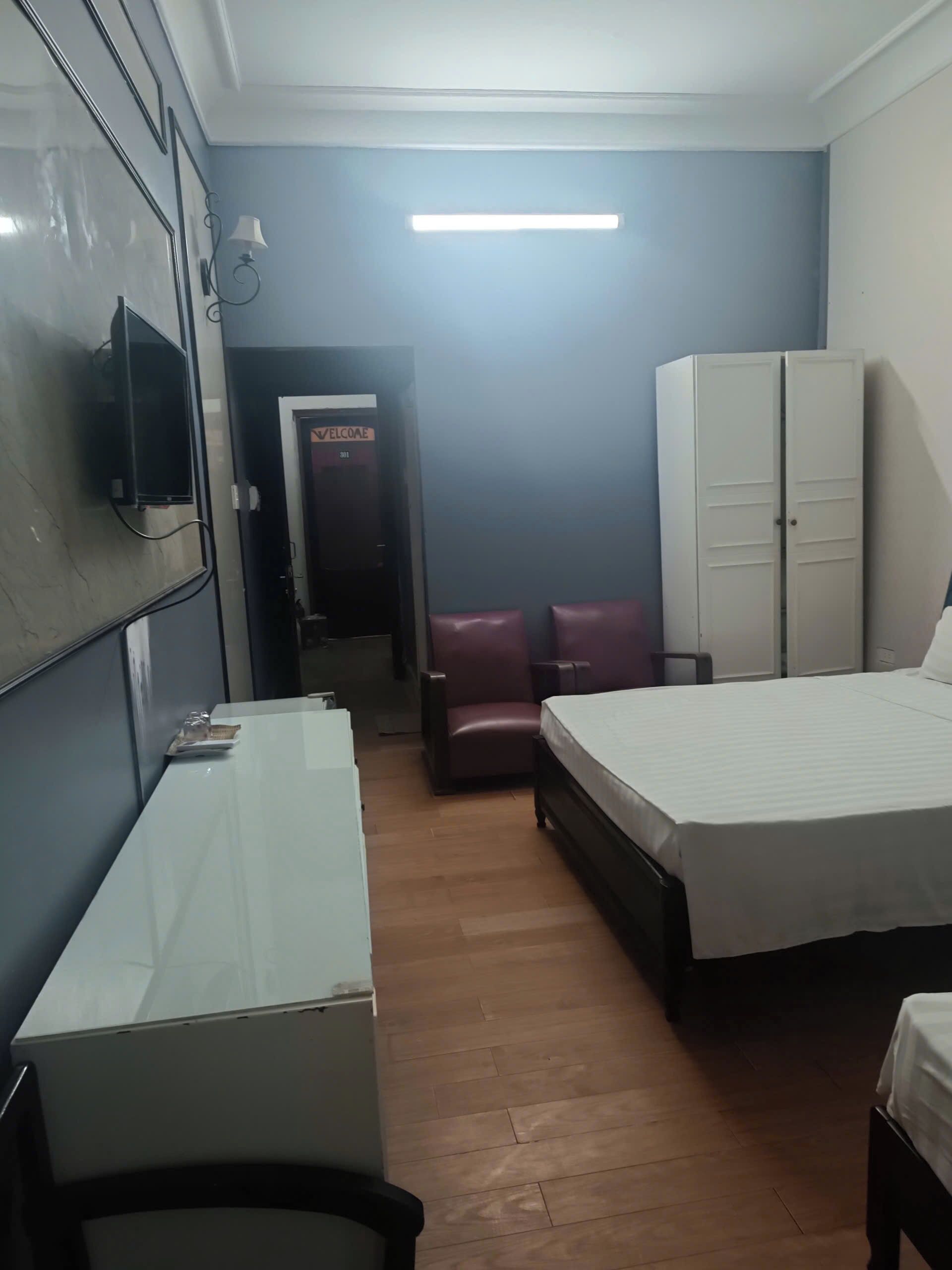 A hotel room with a bed, a desk, a wardrobe, and a television mounted on the wall.