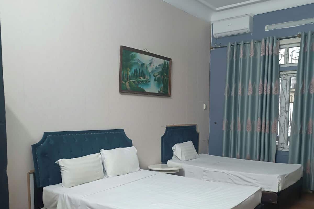 A hotel room with two beds, a painting on the wall, and a window with curtains.