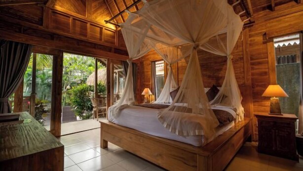 A wooden room with a four-poster bed, a small table, and a lamp. - Bije Suite Villa Ubud (Bali)