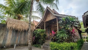 A traditional wooden house with a thatched roof, surrounded by lush tropical vegetation and a stone pathway. - Bije Suite Villa Ubud (Bali)