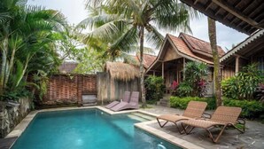 A pool with lounge chairs, surrounded by tropical plants and a thatched-roof structure. - Bije Suite Villa Ubud (Bali)