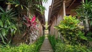 A narrow stone pathway flanked by lush tropical plants leading to a wooden structure with a covered entrance. - Bije Suite Villa Ubud (Bali)