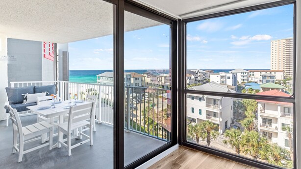 Un balcon avec une table et des chaises, d’où l’on peut admirer l’océan et les bâtiments.