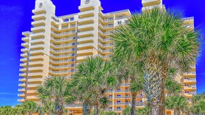 A multi-story hotel with balconies, palm trees in the foreground, and a clear blue sky. - Beachfront Bliss by the Surf | Inlet #605 (New Smyrna Beach)
