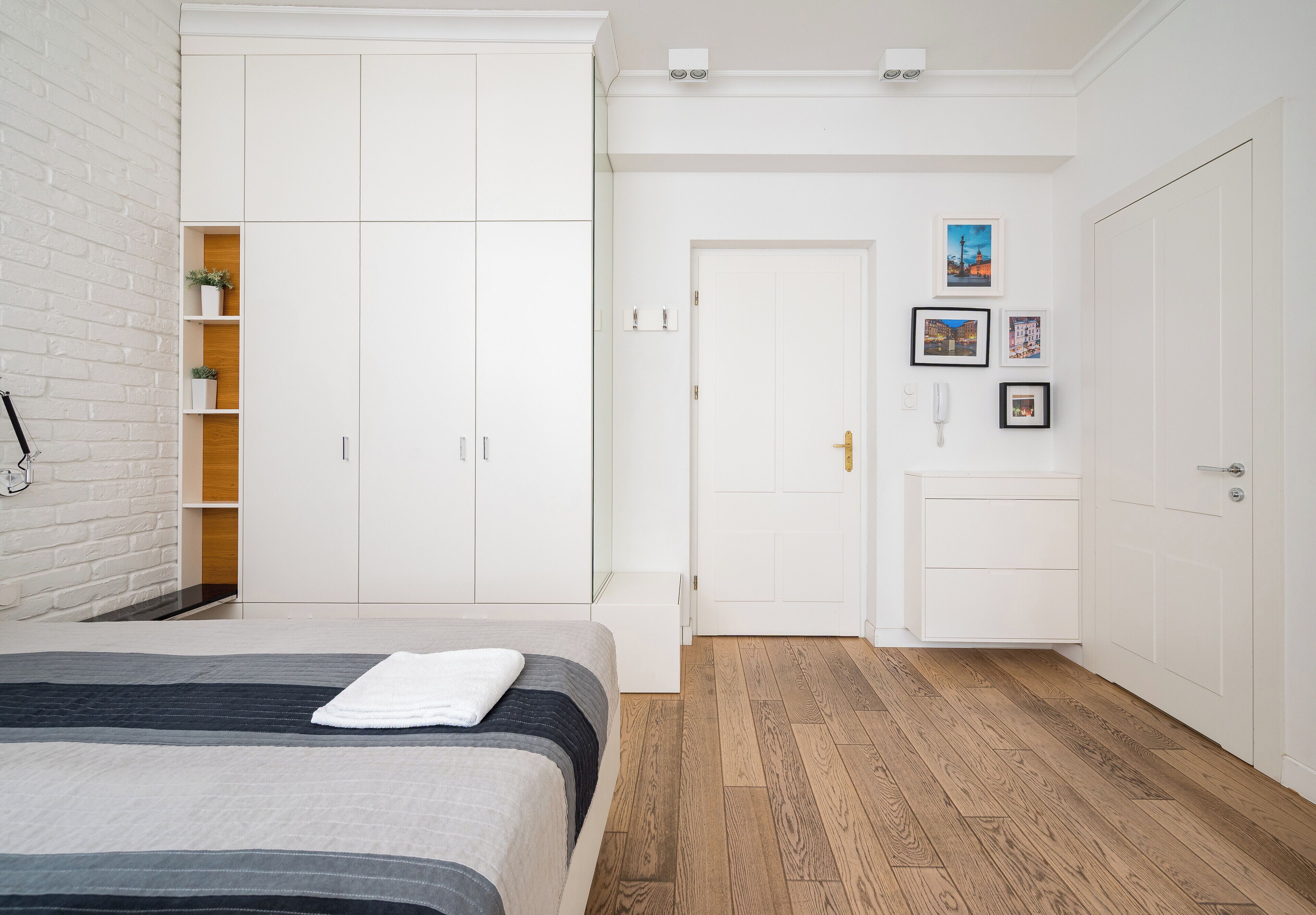 A bedroom with a bed, white wardrobe, wooden flooring, and a door with a view of the outside.