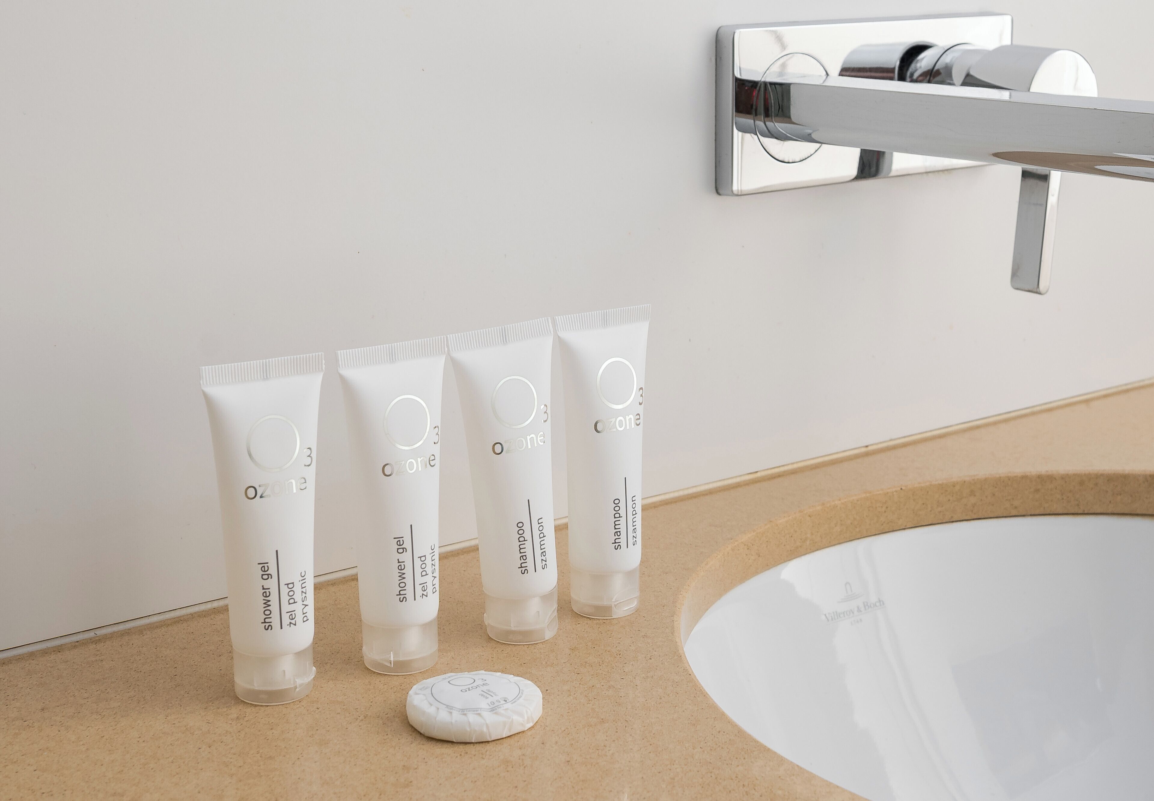 Une salle de bain avec un lavabo blanc, quatre tubes de gel douche blancs et un porte-savon blanc.