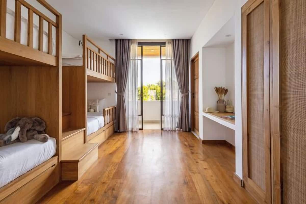 A room with wooden bunk beds, a small desk, and a view through a glass door.