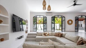 A modern living room with a large L-shaped sofa, a flat-screen TV mounted on the wall, and a ceiling fan. - Villa Harper by BaliSuperHost (Bali)