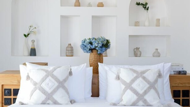 A neatly arranged bedroom with a bed centered between two white shelves, each shelf holding decorative items and a vase with flowers. - Villa Harper by BaliSuperHost (Bali)