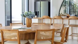 A round wooden dining table with eight chairs, a vase with flowers, and a book on the table. - Villa Harper by BaliSuperHost (Bali)