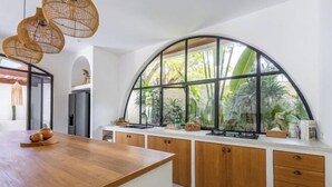 A modern kitchen with a large island, wooden cabinets, and a large window with a view of greenery. - Villa Harper by BaliSuperHost (Bali)