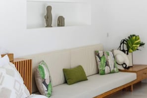 Una sala de estar moderna con un sofá, cojines, una mesita de madera y una planta en maceta.