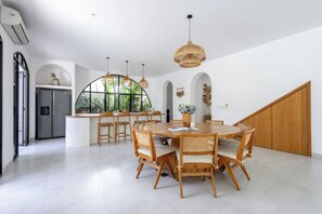 A spacious dining area with a round wooden table and chairs, surrounded by white walls and large windows.