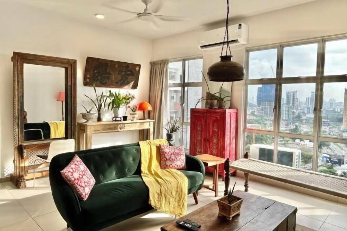 A living room with a green sofa, a wooden coffee table, and a view of the city through large windows.