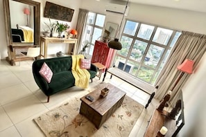 A living room with a green sofa, a wooden coffee table, and a large window with a city view.