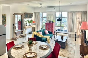 A spacious living area with a dining table, red chairs, a sofa, and a view of the city.