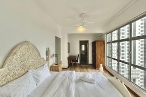 A bedroom with a large bed, a wooden headboard, a nightstand, a window with a view of buildings, and a door leading to another room. - 3BR KL Sentral L21 Modern Vintage City View (Kuala Lumpur)