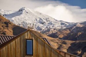 Una montaña con cumbre nevada y un edificio de madera con una ventana en primer plano.