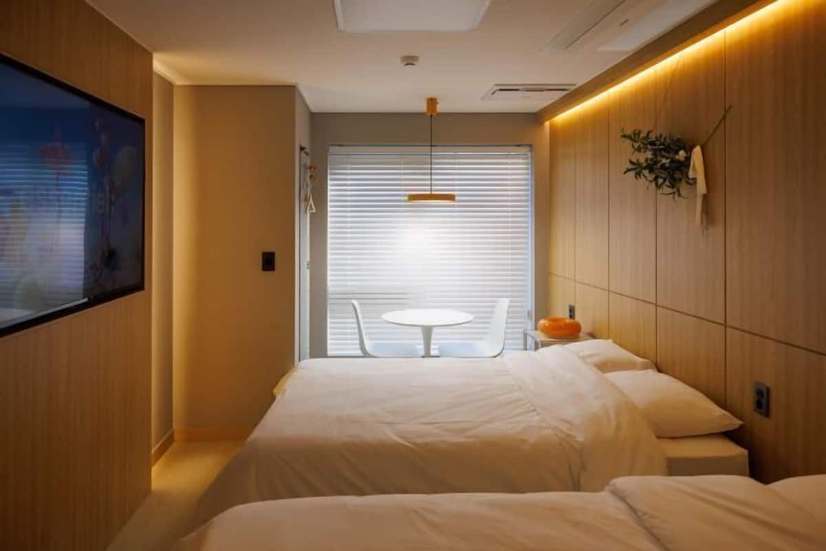 A hotel room with a bed, bedside table, and a window with blinds.