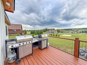 A deck with a barbecue grill and propane tank, overlooking a grassy area and houses. - NEW Construction! Free Community Golf and More (Swanton)