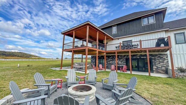 A modern two-story house with a covered outdoor patio, multiple Adirondack chairs, and a fire pit.