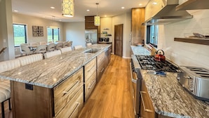 A modern kitchen with a large island, stainless steel appliances, and a dining area with chairs.