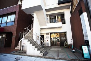 A multi-story building with a staircase leading to the entrance, a visible fire alarm, and a signboard on the sidewalk. - Tokyo Asakusa House (Tokyo)