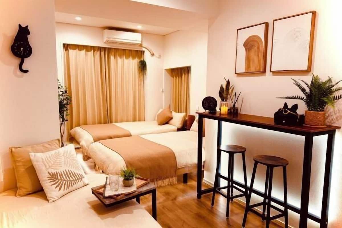 A hotel room with two beds, a small bar area with stools, a cat wall decoration, and framed artwork on the wall.