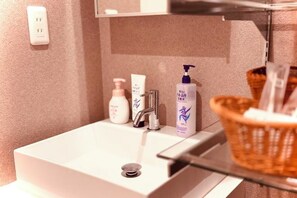 A bathroom with a white sink, a mirror, and toiletries on the countertop. - Tokyo Asakusa House (Tokyo)