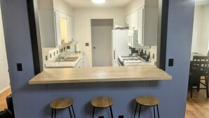 A kitchen with a central island, a sink, and a stove. There are three stools in front of the island. - Game Day Getaway 2 – Easy Walk to OSU Stadium (Stillwater)