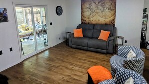 A living room with a grey sofa, orange cushions, a patterned armchair, a world map on the wall, and a sliding glass door leading to an outdoor area. - Game Day Getaway 2 – Easy Walk to OSU Stadium (Stillwater)