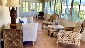 A sunlit room with a sofa, two armchairs, a wooden side table, and a rocking chair. Large windows offer a view of greenery outside. - 
Your Borrego Bungalow: 2BR/2BA at Roadrunner Golf and C.C. Golf cart included! (Borrego Springs)
