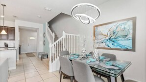 A modern dining area with a glass table, grey chairs, and a staircase leading to another room. - Spacious 5BR Villa w/ Private Pool – near Disney! (Kissimmee)