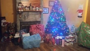Un salon chaleureux avec une cheminée, un sapin de Noël et divers cadeaux emballés.