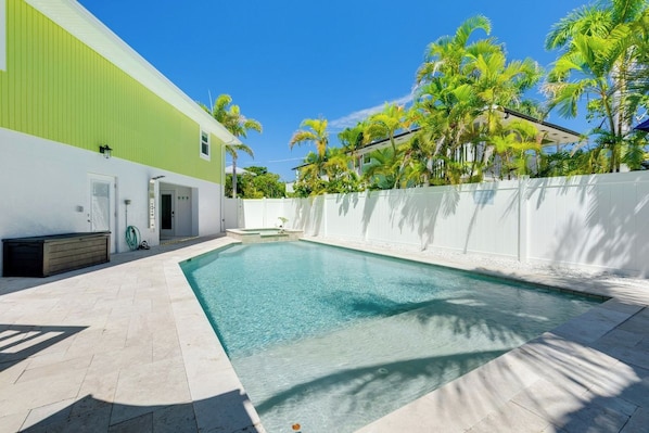 A swimming pool with a white fence, a green building, and palm trees.