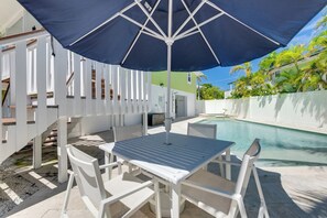 Et poolområde med et bord, stole og en stor parasol, samt en pool.