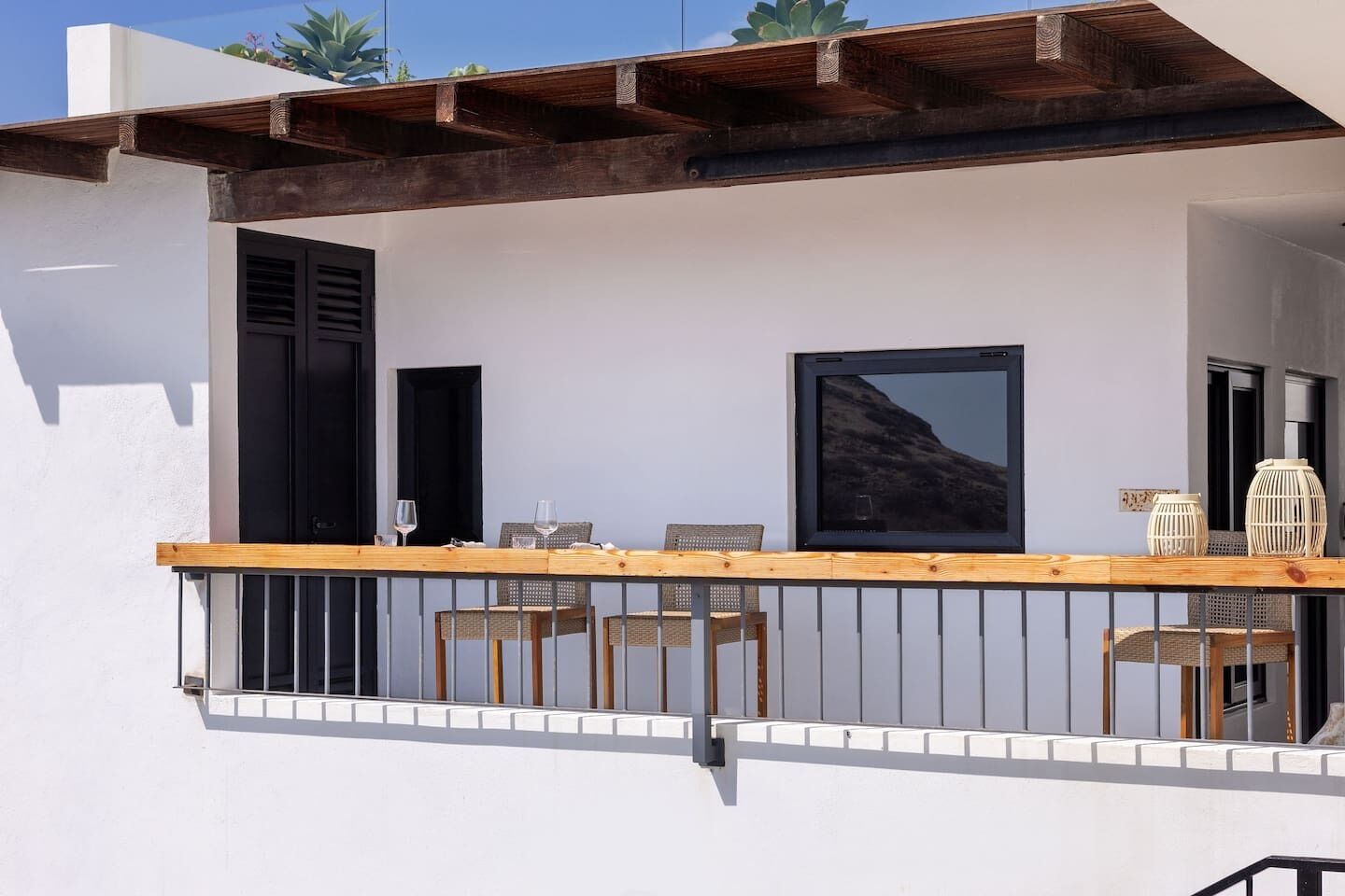 A balcony with a wooden table and chairs, a TV screen, and two doors.