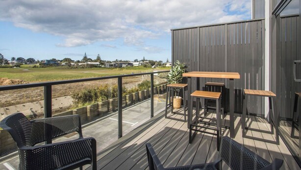 A deck with outdoor seating and a view of a field. - Unwind and Relax in Central Waihi Beach (#B4) (Waihi Beach)