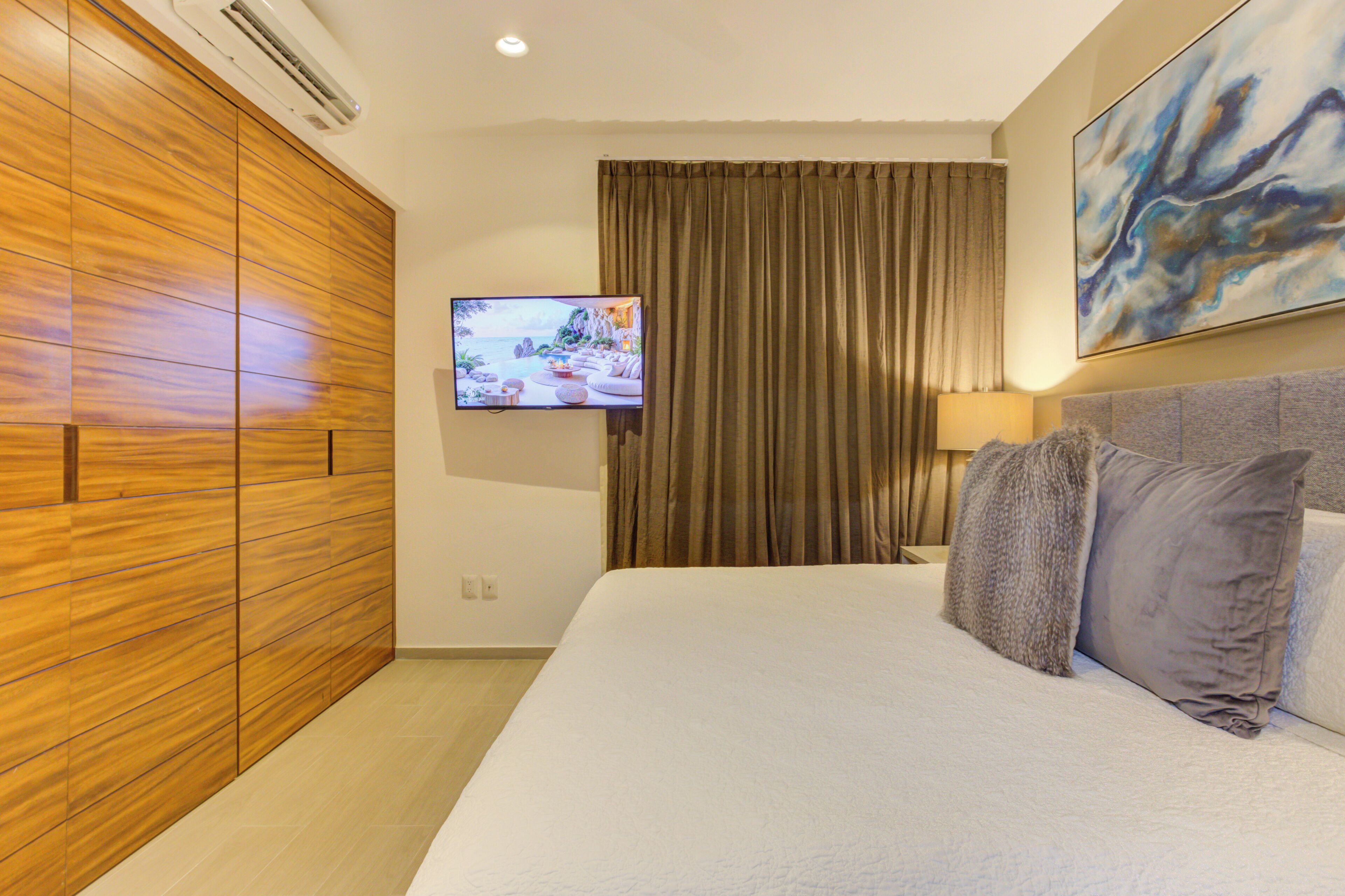 Una habitación de hotel con una cama grande, televisión, armario y un cuadro en la pared.