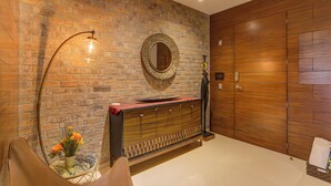 Une pièce avec un mur en briques, un mur recouvert de lambris en bois, un miroir rond, une armoire en bois et un lampadaire.
