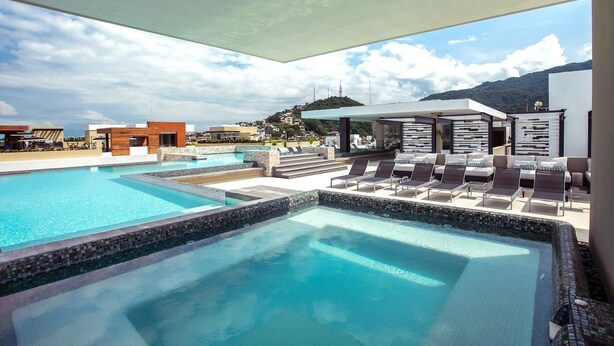 Un espace piscine sur le toit, comprenant plusieurs piscines, des chaises longues et un espace salon couvert.