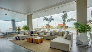 Un salon spacieux, doté d’un grand canapé d’angle, d’une table basse et offrant une vue sur le paysage urbain grâce à de grandes fenêtres.